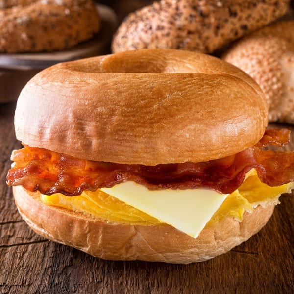 Bagel breakfast sandwich with crispy bacon, scrambled egg, and cheese on a wooden surface.
