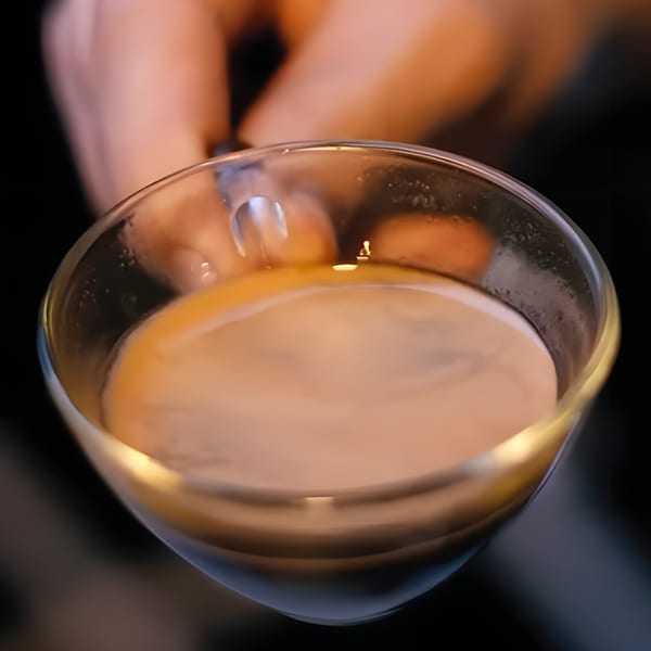 Close-up of a hand holding a glass of Cafezinho, a Brazilian coffee drink.
