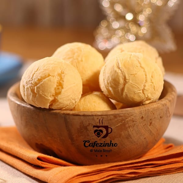 A wooden bowl filled with golden-brown Brazilian cheese bread (pão de queijo) on an orange napkin.