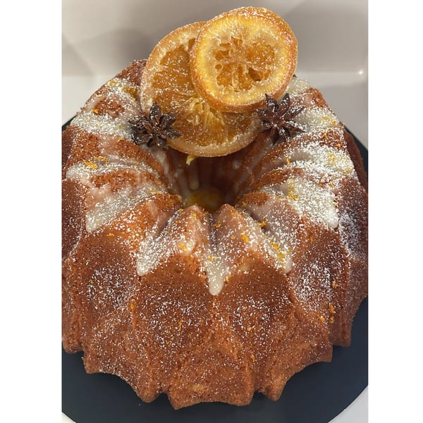 A bundt cake with white icing, powdered sugar, candied orange slices, and star anise on top.