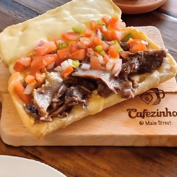 A Brazilian Pão na Chapa with steak, cheese, tomatoes, and onions on a wooden board.