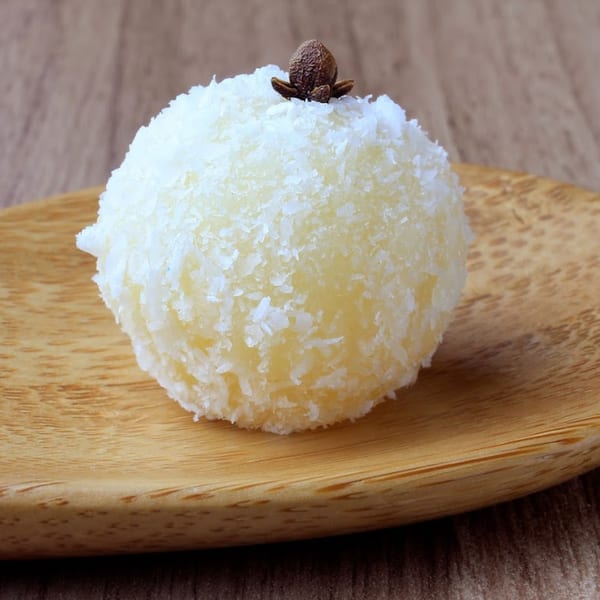 A Brazilian Beijinho de Coco, a white coconut truffle, topped with a clove on a wooden board.